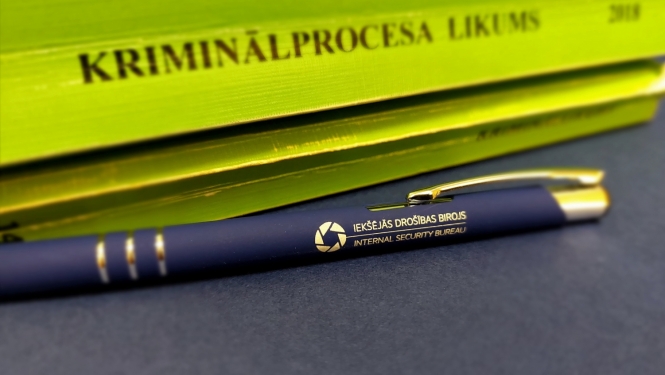 Attēls ar Kriminālprocesa likuma grāmatu zaļā krāsā un zilu pildspalvu ar uzrakstu Iekšējās drošības birojs 