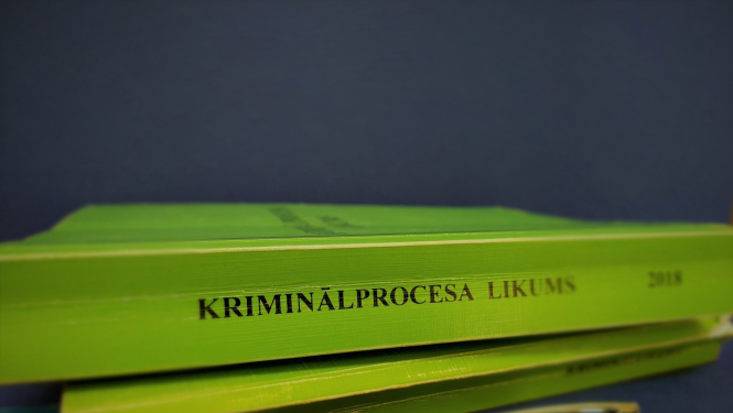 Foto ar Kriminālproces likums grāmatu zaļā krāsā un zilu pildspalvu ar Iekšējās drošības biroja logo