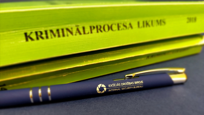 Attēls ar Kriminālprocesa likuma grāmatu zaļā krāsā un zilu pildspalvu ar uzrakstu Iekšējās drošības birojs 