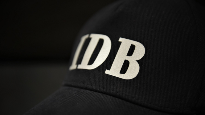 Attēls ar melnu cepuri un gaišiem burtiem IDB uz tās