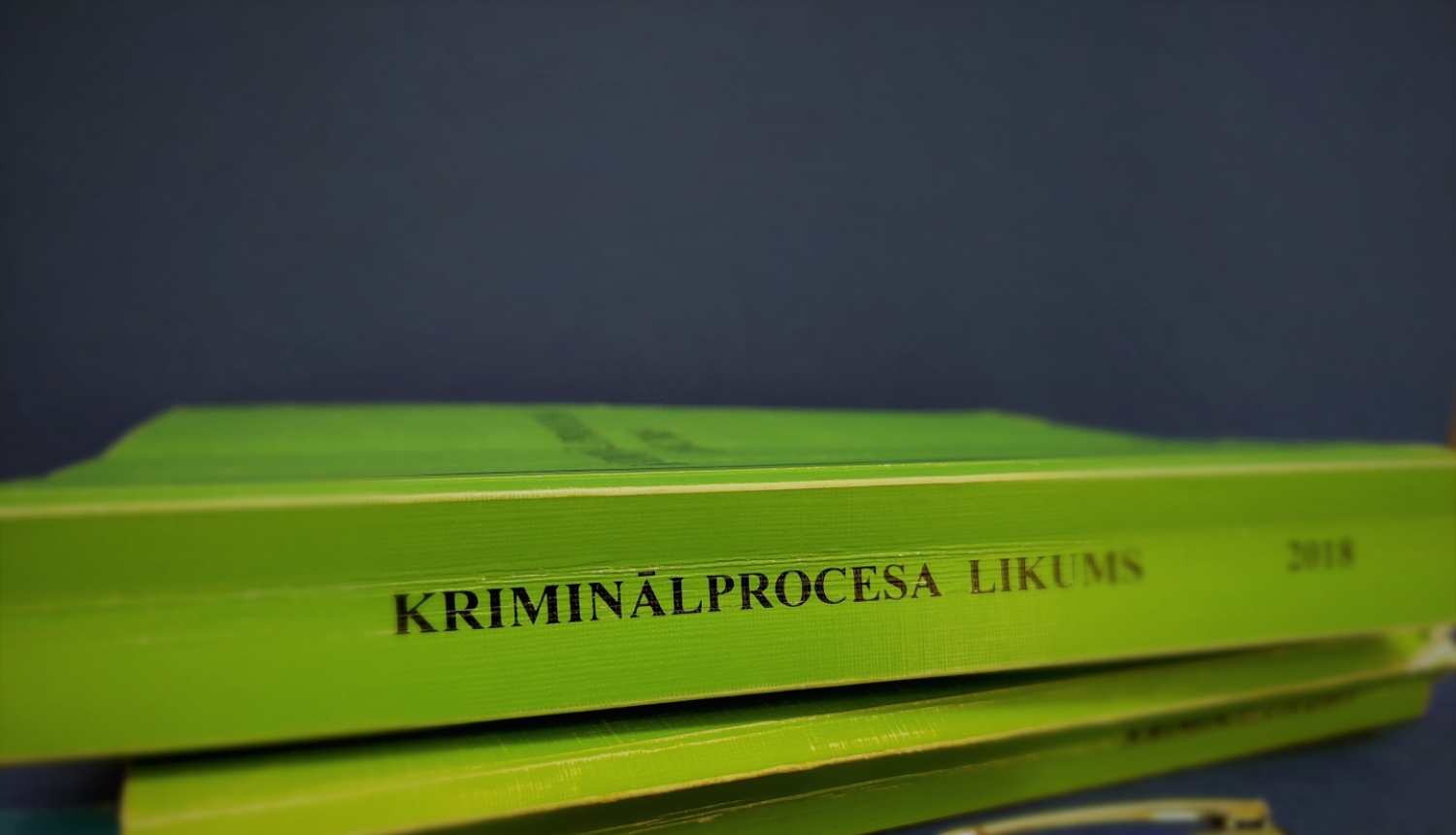Foto ar Kriminālproces likums grāmatu zaļā krāsā un zilu pildspalvu ar Iekšējās drošības biroja logo