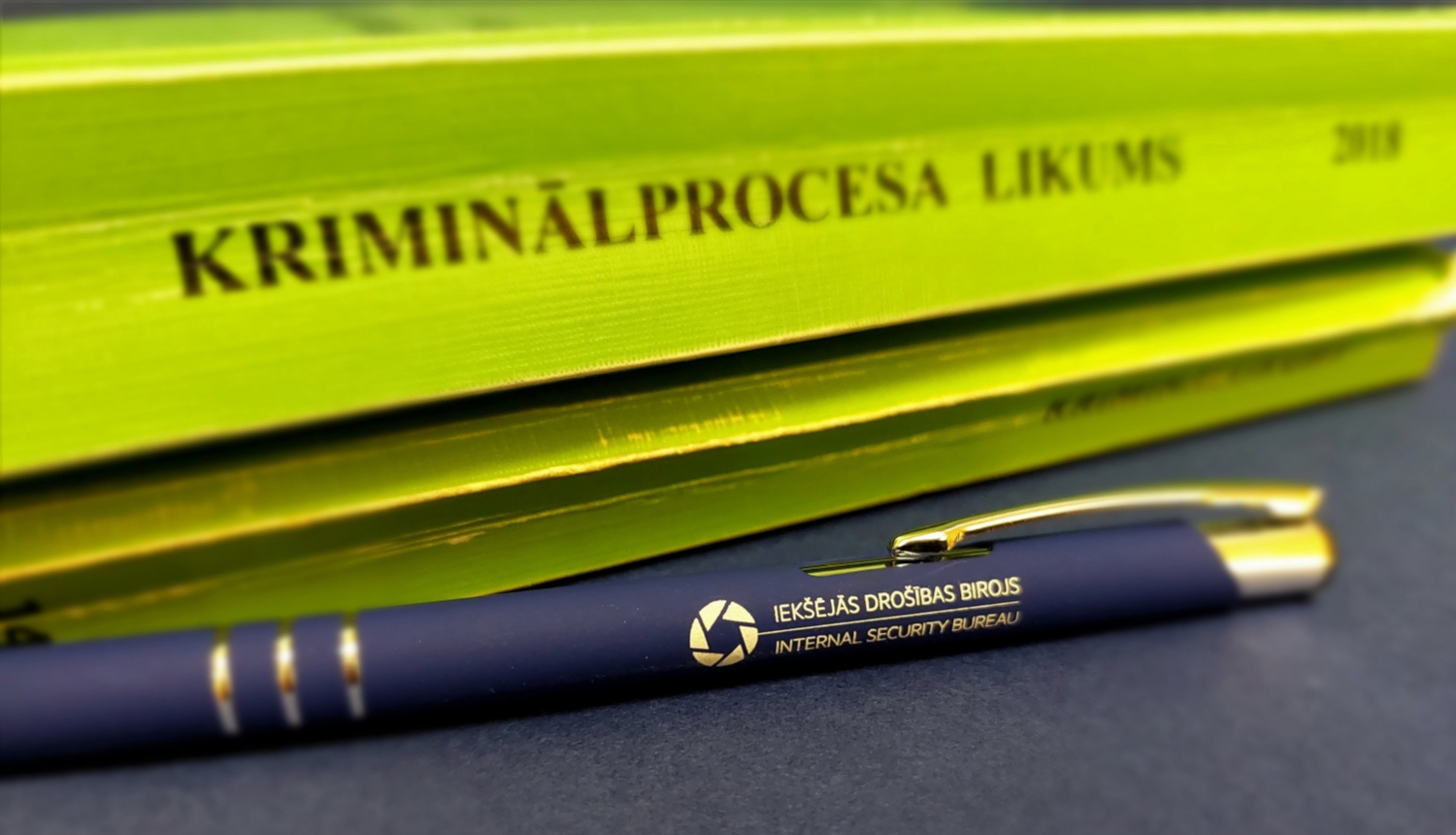 Attēls ar Kriminālprocesa likuma grāmatu zaļā krāsā un zilu pildspalvu ar uzrakstu Iekšējās drošības birojs 