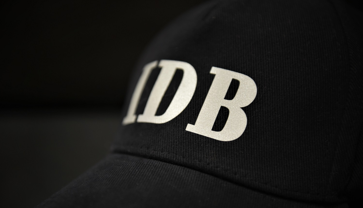 Attēls ar melnu cepuri un gaišiem burtiem IDB uz tās